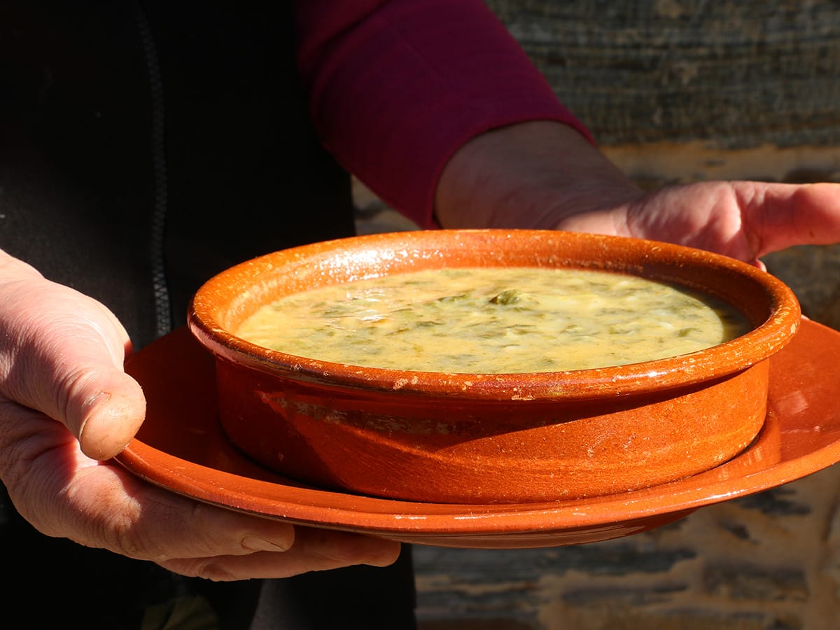 Persoa suxeitando un prato de caldo galego en cunca de barro