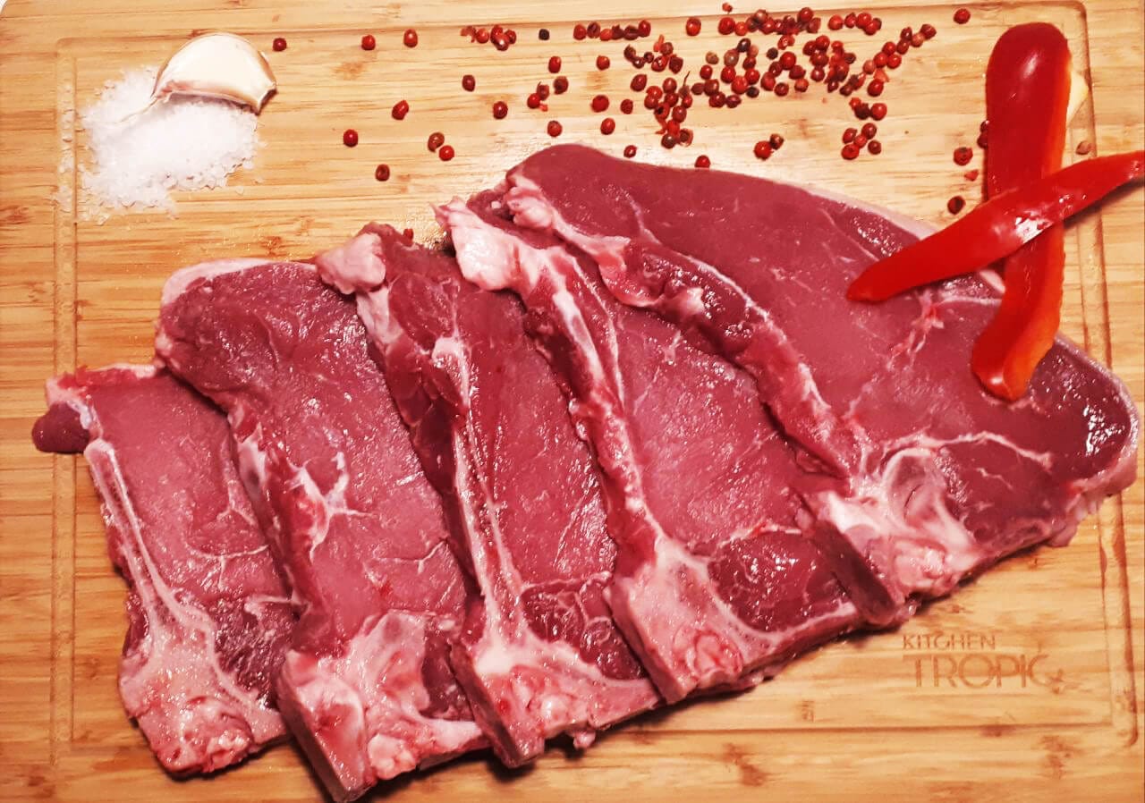 Chuletas de tenreira cruas cortadas sobre táboa de madeira