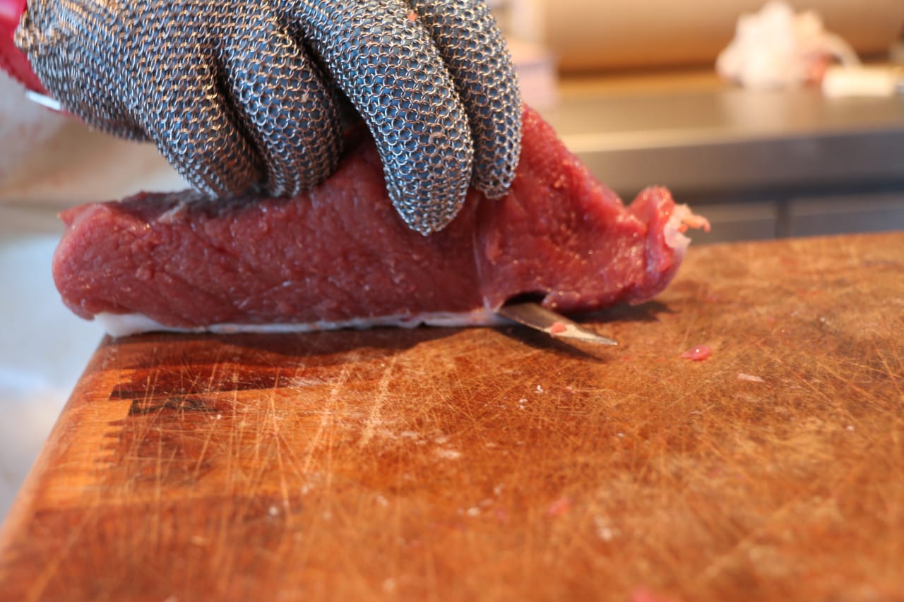 Man enluvada cortando unha peza de carne de vacún nunha táboa