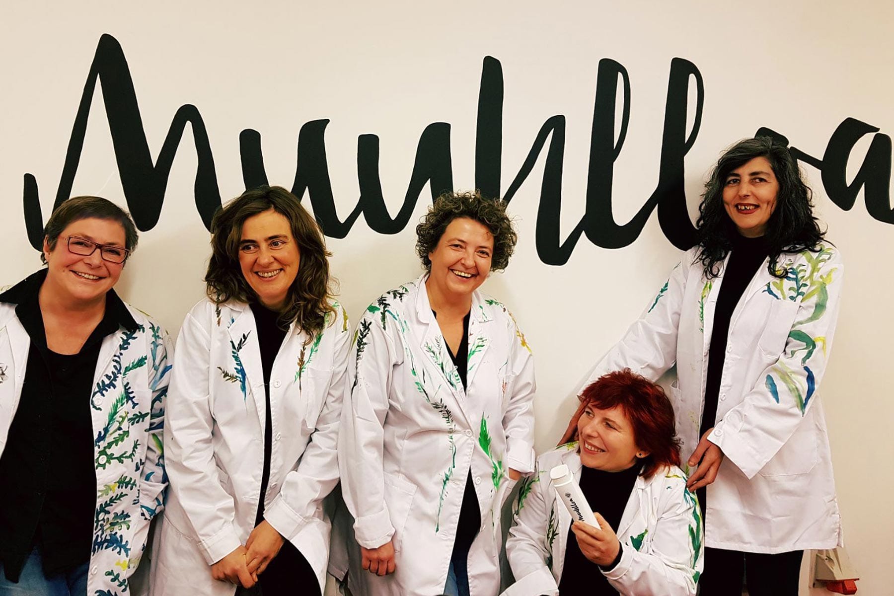 Equipo de Muuhlloa sorrindo con bata branca diante do logotipo